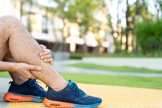 Male runner athlete leg injury and pain. Hands grab painful leg while running in the park.