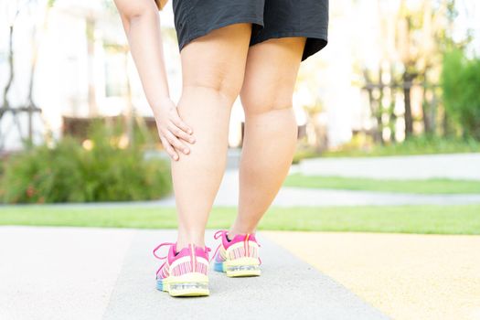 Female fatty runner athlete leg injury and pain. Hands grab painful leg while running in the park.