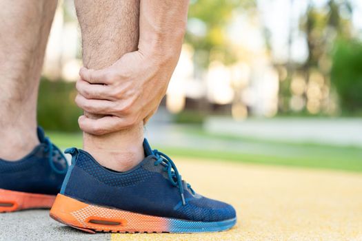 Male runner athlete leg injury and pain. Hands grab painful leg while running in the park.