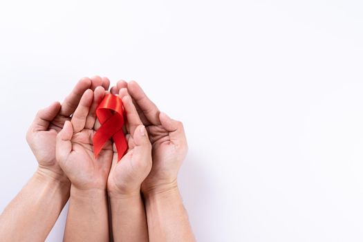 Aids awareness, man and woman hands holding red ribbon on white background with copy space for text. World Aids Day, Healthcare and medical concept.