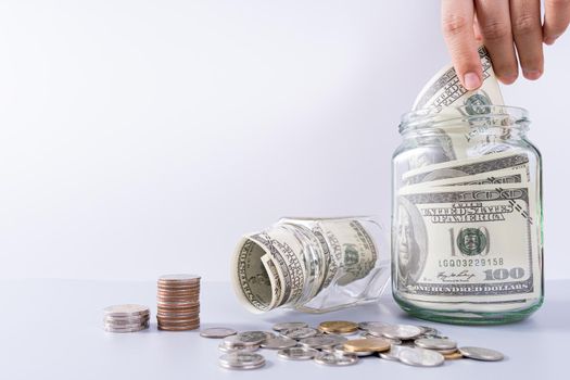 Hand putting money paper into jar with stack coins isolated grey background. Property investment and house mortgage financial concept.