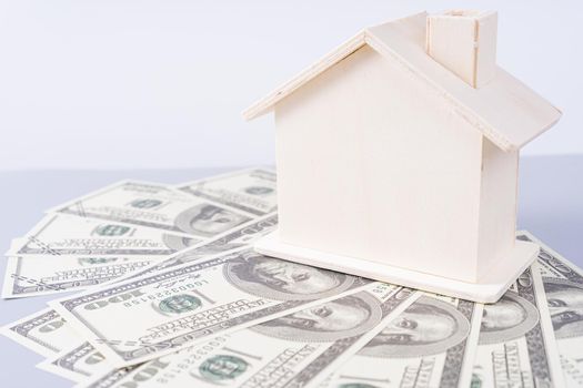 Wooden house and a pile of money paper isolated grey background. Property investment and house mortgage financial concept.