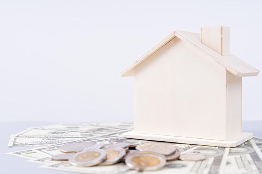 Wooden house and a pile of money coins and paper isolated grey background. Property investment and house mortgage financial concept.