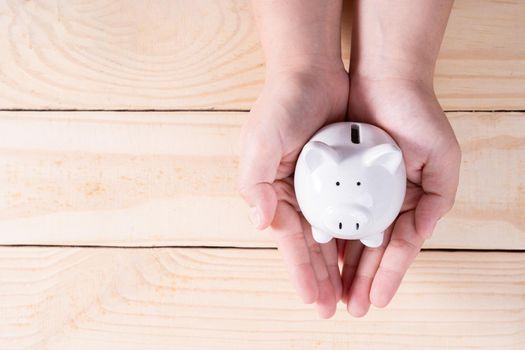 Hands hold a piggy bank on wooden background. Saving money and investment concept.