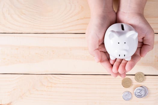 Hands hold a piggy bank with a pile of coins on wooden background. Saving money and investment concept.