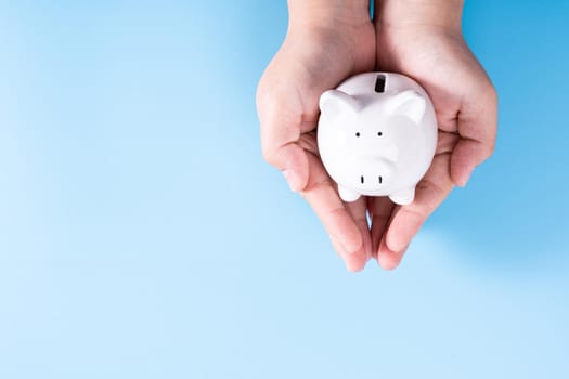 Hands hold a piggy bank isolated blue background. Saving money and investment concept.