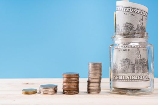 Money paper inside jar and stack coins isolated blue background. Property investment and house mortgage financial concept.