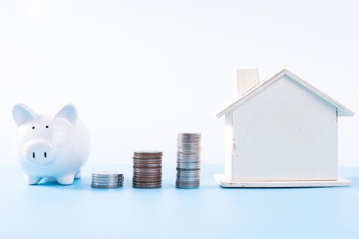 Piggy bank with wooden house and stack coins isolated grey background. Property investment and house mortgage financial concept.