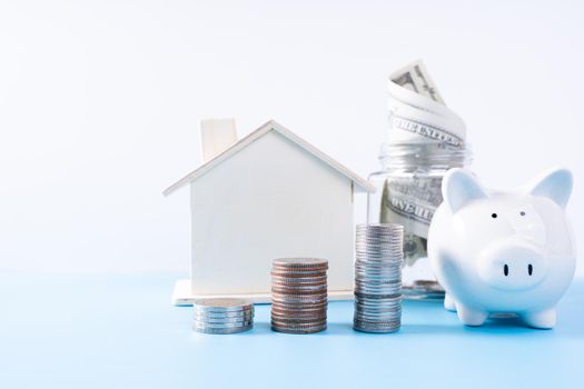 Piggy bank with wooden house and stack coins and money paper inside jar isolated grey background. Property investment and house mortgage financial concept.