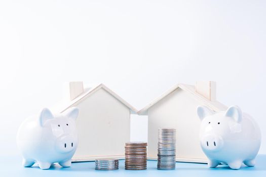 Piggy bank with wooden house and stack coins isolated grey background. Property investment and house mortgage financial concept.