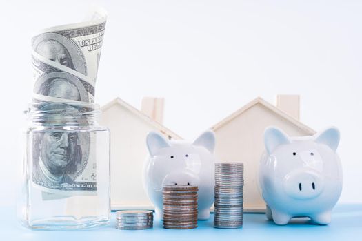 Piggy bank with stack coins and money paper inside jar and wooden house isolated grey background. Property investment and house mortgage financial concept.