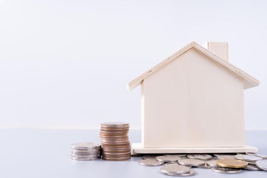 Wooden house with stack coins isolated grey background. Property investment and house mortgage financial concept.