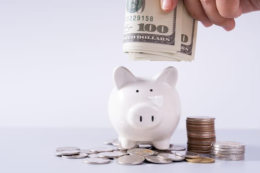 Hand putting money paper into piggy bank with stack coins isolated grey background. Saving money and investment concept.