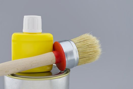 Clean bristle brush and yellow pigment jar on tin of paint over a grey background. New color, decorating or renovations concept