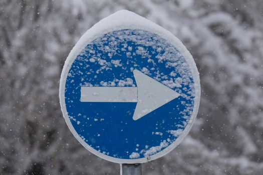 Madrid, Spain - January 09, 2021: A mandatory one-way traffic sign, covered with snow in the Retiro district, on a snowy day, due to the Filomena polar cold front.