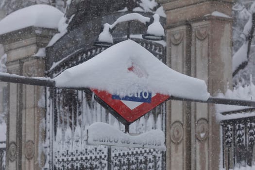 Madrid, Spain - January 09, 2021: Subway entrance and Metro sign, Bank of Spain stop in Alcala street, on a snowy day, due to the Filomena polar cold front.