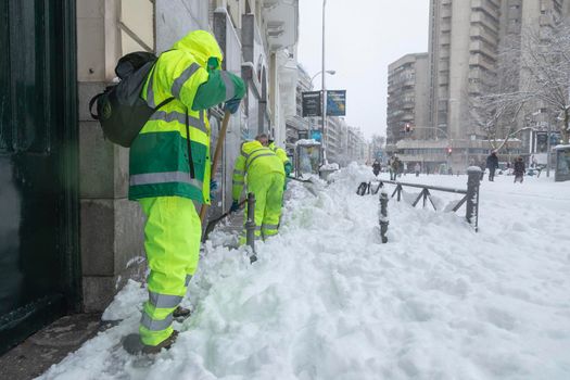 Madrid, Spain - January 09, 2021: A group of workers from the municipal cleaning service work cleaning the sidewalks with shovels and salt, due to the filomena polar cold front.