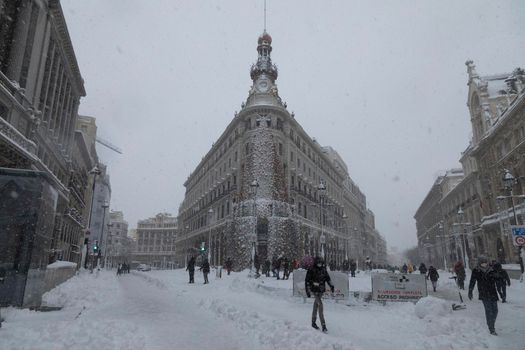 Madrid, Spain - January 09, 2021: People walking in front of the Four Seasons hotel, decorated with a giant Christmas tree, on a snowy day, due to the polar cold Filomena front.