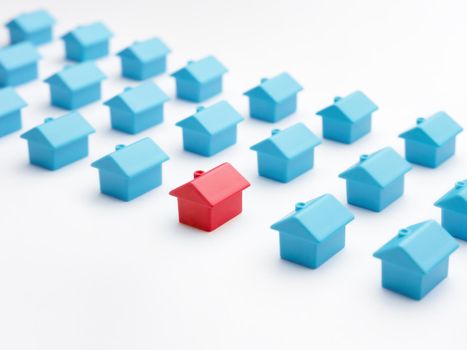 Home choice or selection property and real estate. Red house model among blue toy houses on white color background. Unique house different from group of same type miniature houses. Property marketing