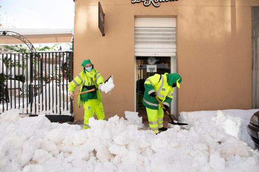 Madrid, Spain - January 10, 2021: Woman worker from the municipal cleaning service work cleaning the sidewalks with shovels and salt, due to the filomena polar cold front.