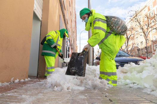 Madrid, Spain - January 10, 2021: Women workers from the municipal cleaning service work cleaning the sidewalks with shovels and salt, due to the filomena polar cold front.