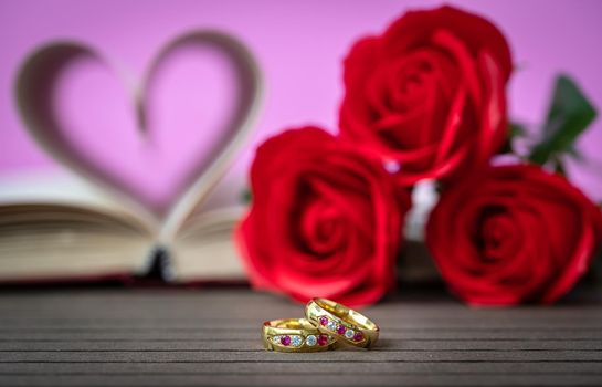 Pages of book curved into a heart shape with red rose and wedding ring . Love concept of heart shape from book pages