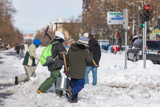 Madrid, Spain - January 10, 2021: Citizens and neighbors of Madrid, collaborating and cleaning the snow from the streets and highways, on a snowy day, due to the Filomena polar cold front.