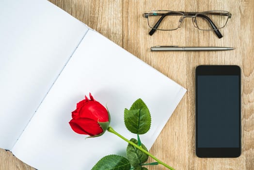 Top view shot of red roses empty blank notebook diary and eye glasses with smartphone on wood table,Valentine concept