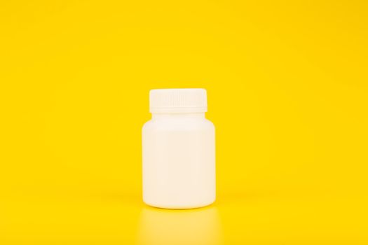 Minimalistic still life white plastic medication bottle against yellow background with copy space. Simple and creative concept of pharmacy, medical treatment or vitamins for kids. 