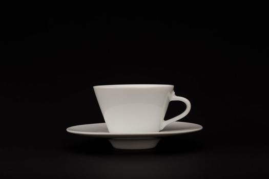 Minimalistic still life with white ceramic coffee cup on plate against black background with copy space. High quality photo