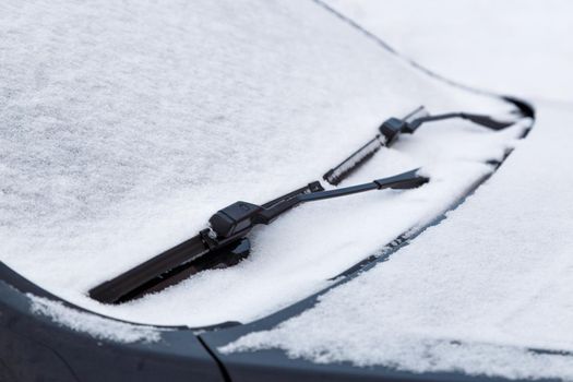 car windshield and wiper waterblades frozen and covered with snow at winter cloudy day light with selective focus and background blur