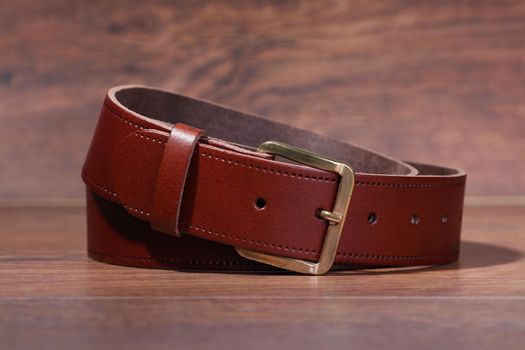 A leather brown belt rolled up on a wood background