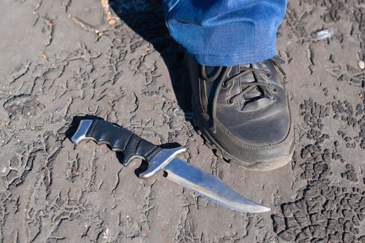 the knife is lying on the ground next to the foot of a man in black sneakers