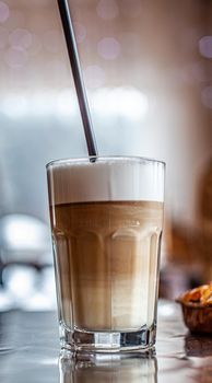 Hot Latte coffee in a glass and a fresh apple dessert next to it. The hot drink is served with a plastic straw. Delicious breakfast in the cafe