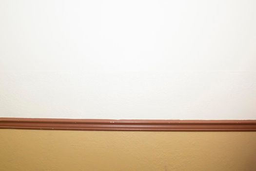 Blank white and tan wall separated by brown moulding