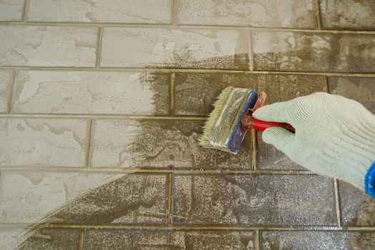 A construction worker applies paint to a brick wall.The painter paints primers the walls with a brush, makes repairs in the house or room.Reconstruction of the building, specialist restores the wall                               