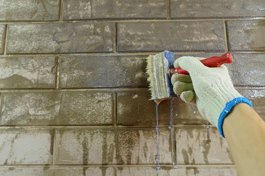 A construction worker applies paint to a brick wall.The painter paints primers the walls with a brush, makes repairs in the house or room.Reconstruction of the building, specialist restores the wall