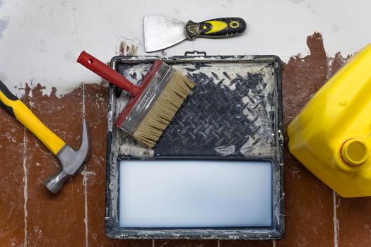 A hammer,a spatula,a paint brush,a canister and a tray for paints lie on the floor during the repair and restoration of the house.Work as a Builder or handyman in the house.Repairing a room