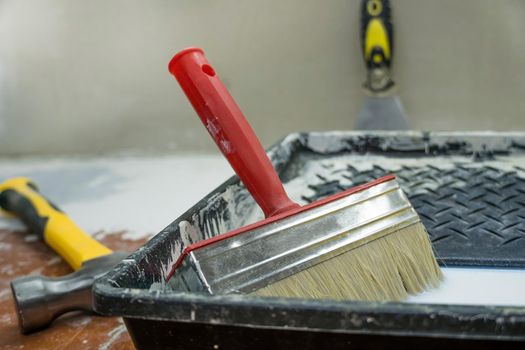 A hammer,a spatula,a paint brush and a tray for paints lie on the floor during the repair and restoration of the house.Work as a Builder or handyman in the house.Repairing a room