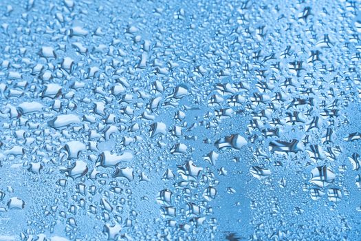 Wet glass with large drops of water or rain of blue color. Background or wallpaper with water texture close-up. Image of water droplets on a clear glass surface during heavy rain