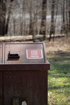 Large rusted receptacle for trash in front of a lake