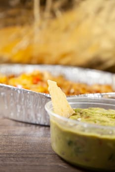 Tortilla chip in a container of guacamole with a tin of food in the background, in a dark, golden fall colors