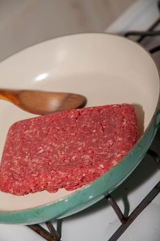 Raw ground beef in a frying pan with a wooden spoon