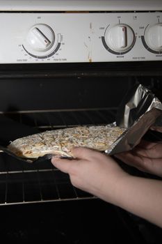 Close up of a woman's hands as they push a baking sheet of a frozen cheese pizza into an oven