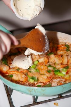 Adding cream cheese to a frying pan with shrimp and green onion