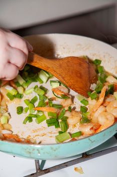 Stirring diced green onion into shrimp cooking on a stove