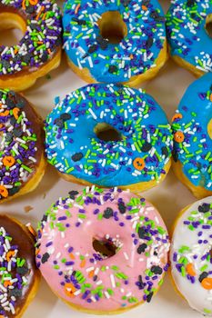 Donuts with brown, blue, pink and white icing covered with multicolored sprinkles in a white box