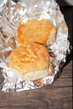 Two buttermilk biscuits on foil on a wooden table