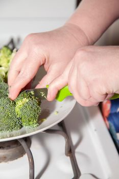 Woman's hands chopping a fresh crown of broccoli