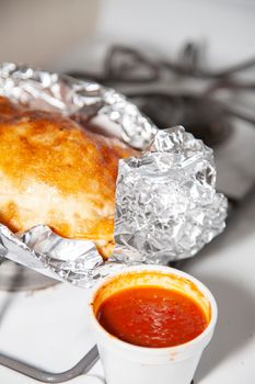 Glazed outter bread of a fresh calzone on foil next to a styrofoam cup of marinara sauce